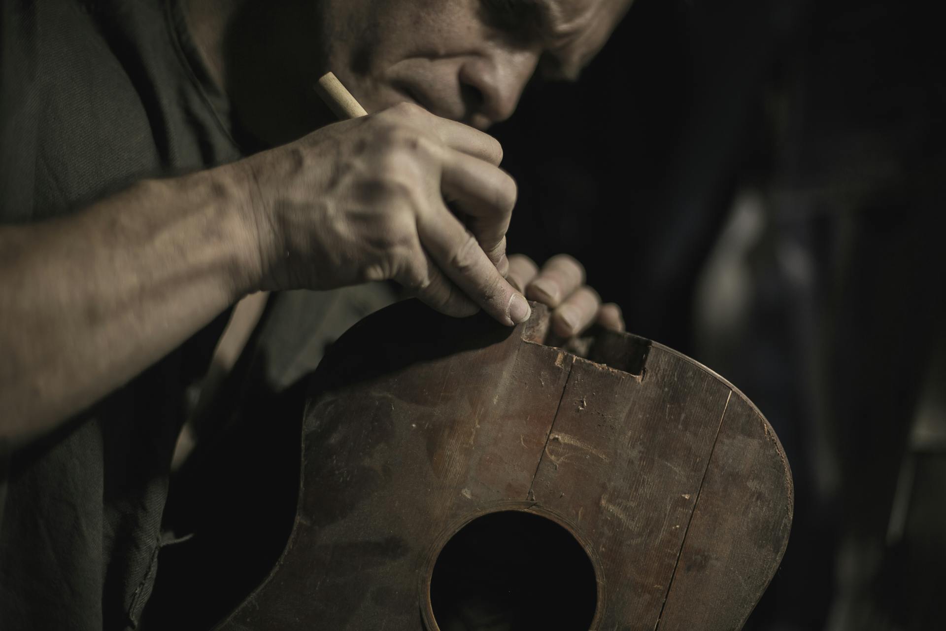 Luthier crafting guitar in moody workshop